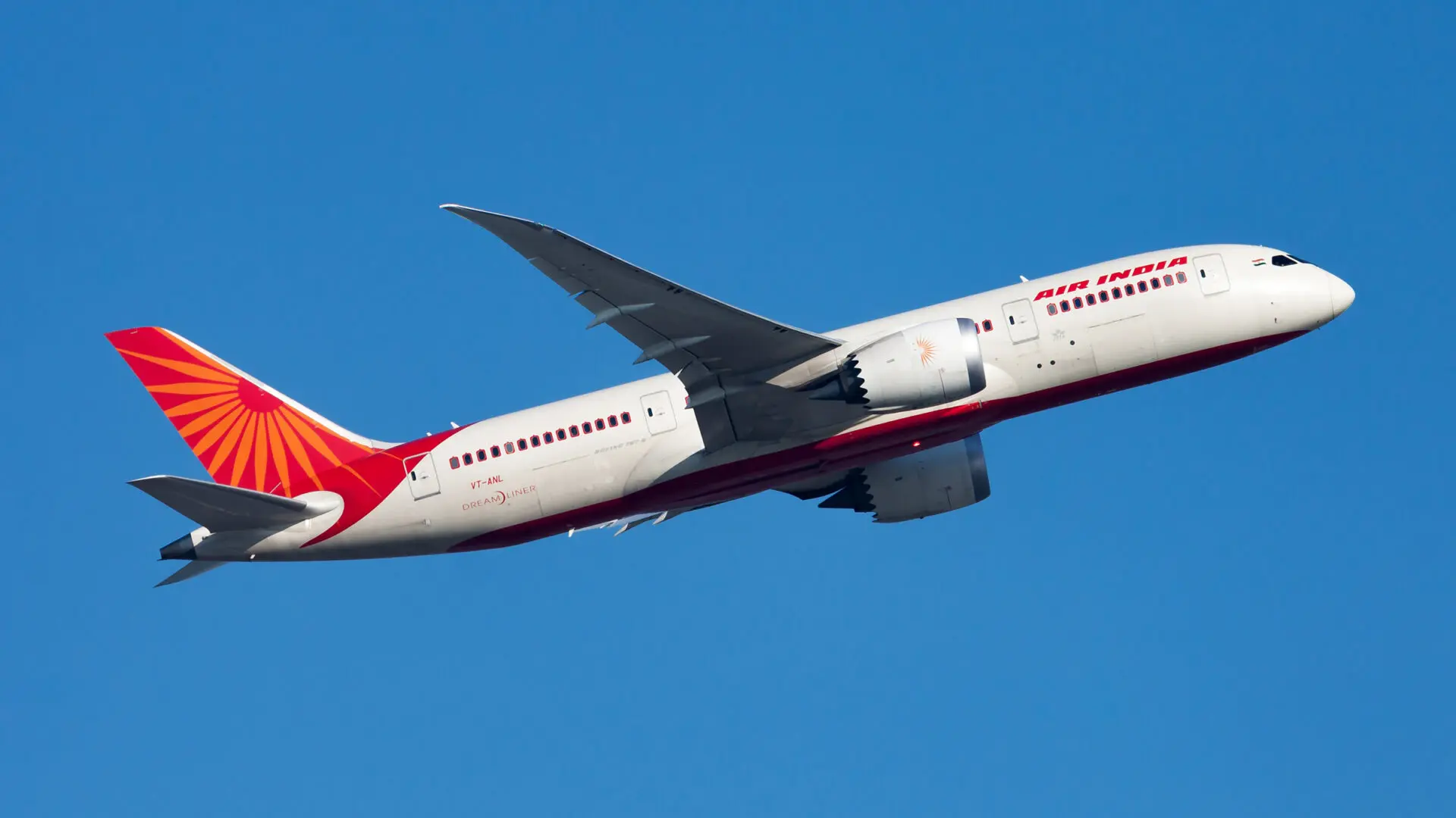 Air India aircraft in white and red livery flying against a clear blue sky angled upward