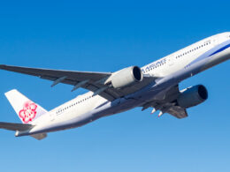 White passenger jet climbs in a clear blue sky with a pink flower logo on the tailfin
