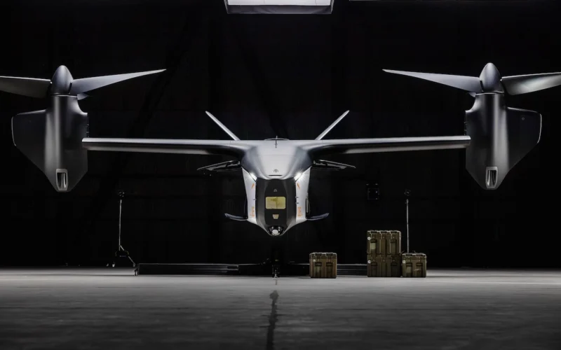 Front on view of a sleek silver eVTOL aircraft in a dark hangar with cargo cases on the floor nearby