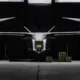 Front on view of a sleek silver eVTOL aircraft in a dark hangar with cargo cases on the floor nearby