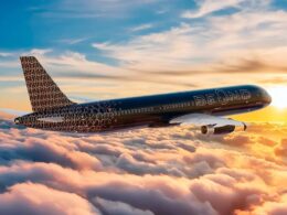 Commercial airplane with a circular pattern livery flies above orange pink clouds at sunset BEOND branding visible on the fuselage