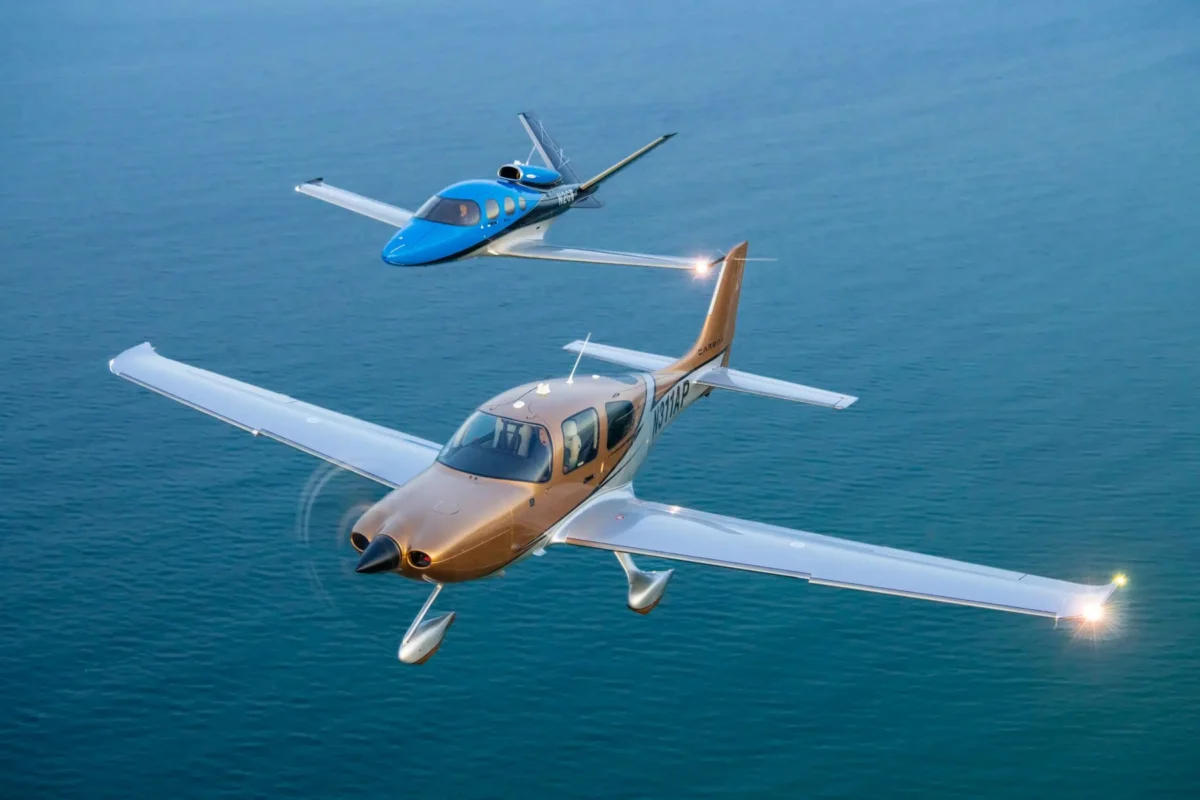 cirrussr22sf50 Two small private airplanes flying in formation over a calm blue ocean with a tan aircraft in the foreground and a blue aircraft behind it