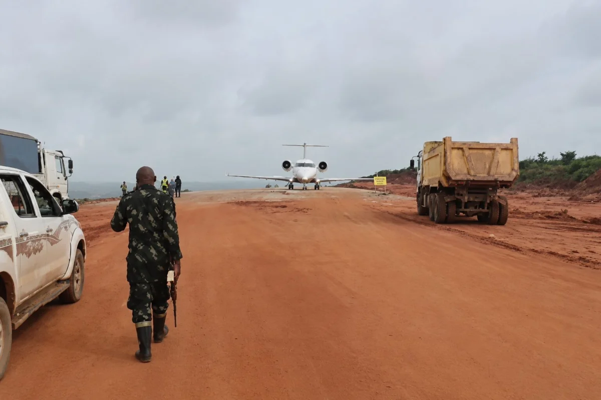 A soldier walks down a red dirt airstrip toward a small white jet with trucks parked on both sides
