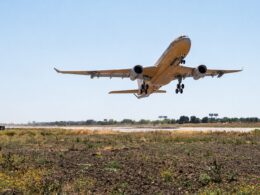 Wide angle shot of a passenger jet taking off from a runway under a bright blue sky landing gear down with dry grassy foreground below