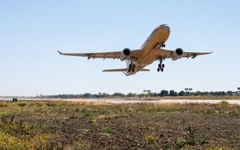 Wide angle shot of a passenger jet taking off from a runway under a bright blue sky landing gear down with dry grassy foreground below