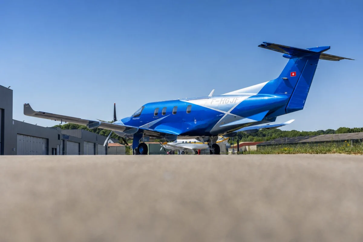 e0444d84 d0a7 4d6d af0c 0aaab37aa72c Blue private jet parked on a tarmac in front of airport hangars under a clear blue sky Swiss flag on tail left visible