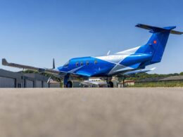 Blue private jet parked on a tarmac in front of airport hangars under a clear blue sky Swiss flag on tail left visible
