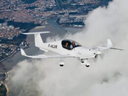 Twoperson white light aircraft in flight over a coastal city with a marina below clouds around it