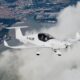 Twoperson white light aircraft in flight over a coastal city with a marina below clouds around it
