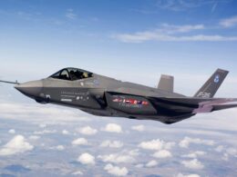 Grey F 35 Lightning II fighter jet in flight above a sea of white clouds nose to the left and cockpit canopy visible