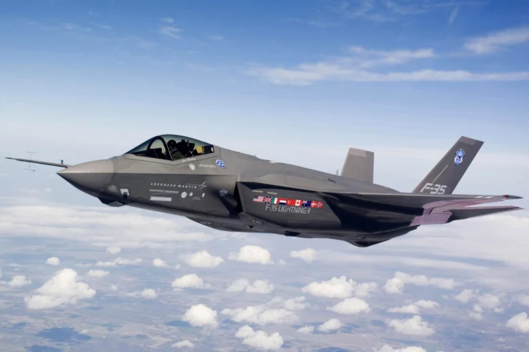 Grey F 35 Lightning II fighter jet in flight above a sea of white clouds nose to the left and cockpit canopy visible