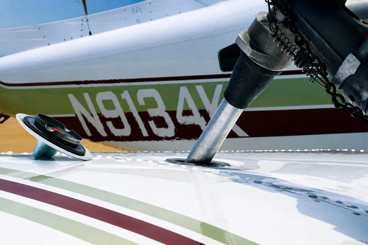 faa avgas Close up of a small airplane wing and landing gear area showing a silver support strut passing through an opening in the wing with a coiled chain and hardware in the background