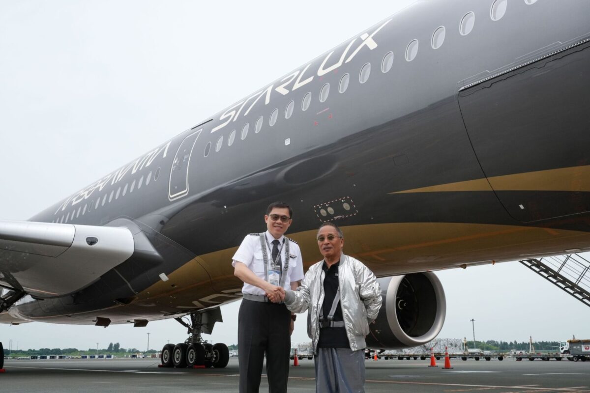 image Two airline crew members shake hands in front of a large gray commercial airliner on the tarmac with engines stairs and ground equipment in the background