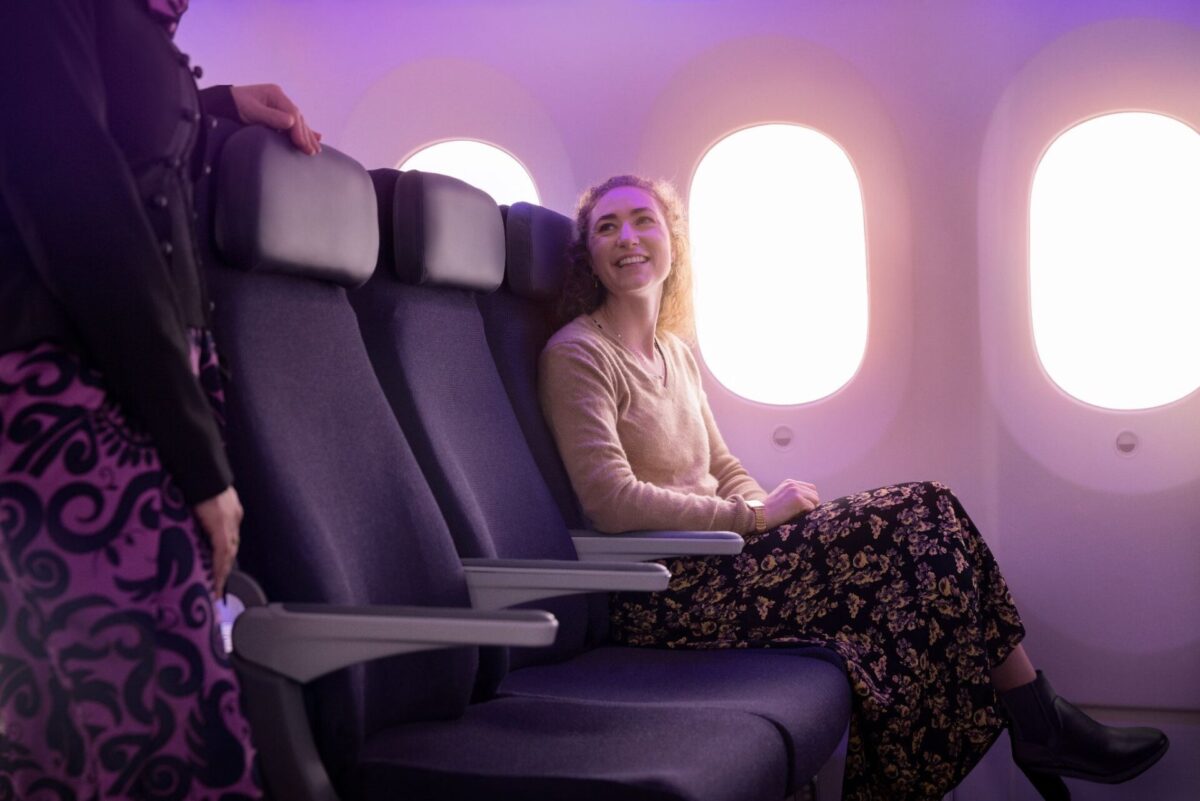 image Woman seated in a purple lit airplane cabin smiling at a standing flight attendant beside her row