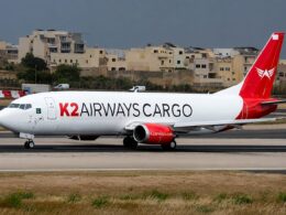 Cargo airplane with K2 AIRWAYS CARGO branding taxiing on a runway near beige buildings in the background overcast sky