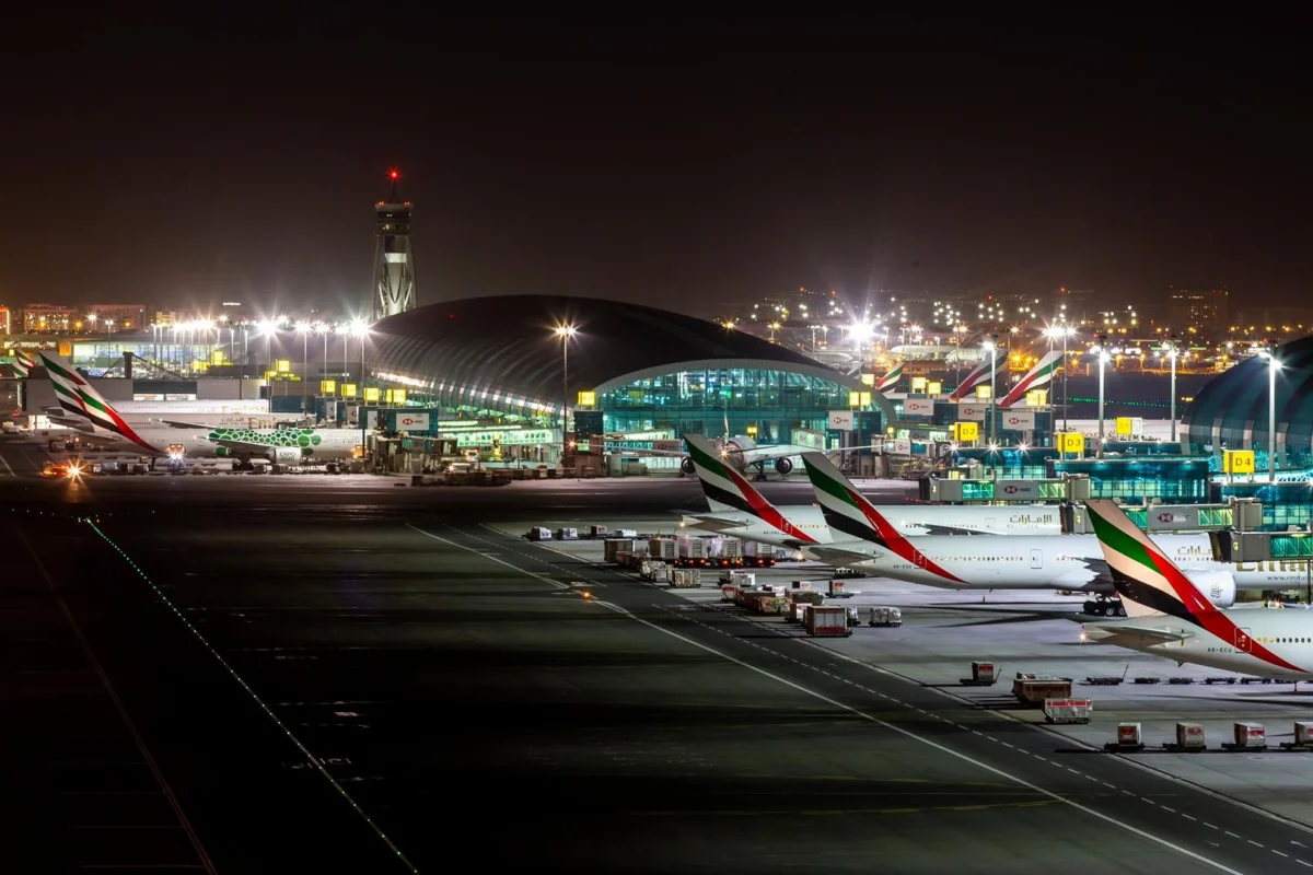 Nighttime airport scene with several Emirates planes parked at gates beside an illuminated terminal building