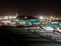 Nighttime airport scene with several Emirates planes parked at gates beside an illuminated terminal building