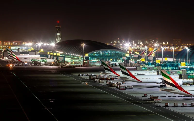 Nighttime airport scene with several Emirates planes parked at gates beside an illuminated terminal building