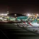 Nighttime airport scene with several Emirates planes parked at gates beside an illuminated terminal building