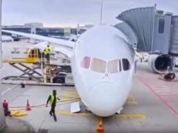 Front view of a white passenger airliner at the gate jet bridge connected and ground crew nearby on the tarmac
