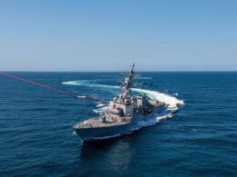 Gray US Navy destroyer sails through deep blue ocean under a clear sky American flag fluttering on the hull