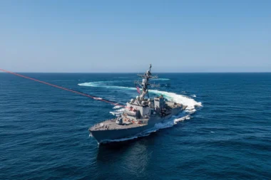 Gray US Navy destroyer sails through deep blue ocean under a clear sky American flag fluttering on the hull
