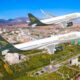 Two Shohin Airlines planes fly in formation over a city with green parks and mountains in the background blue sky overhead