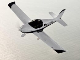 White single engine aircraft with a bubble canopy flying over the ocean registration N511WG visible along the fuselage