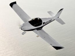 White single engine aircraft with a bubble canopy flying over the ocean registration N511WG visible along the fuselage