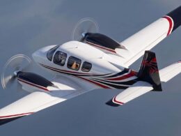 Private twin engine propeller aircraft in level flight with white red and black livery visible cockpit windows and rotating propellers creating motion blur