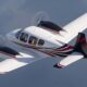 Private twin engine propeller aircraft in level flight with white red and black livery visible cockpit windows and rotating propellers creating motion blur