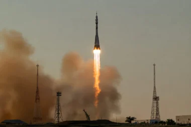 Rocket lifts off from a launchpad flames and smoke trailing as it ascends with tall support towers on the ground below