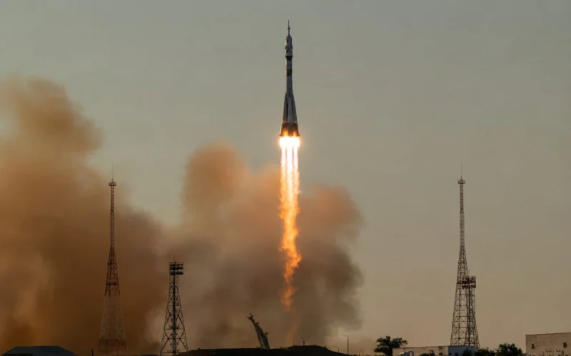 Rocket lifts off from a launchpad flames and smoke trailing as it ascends with tall support towers on the ground below