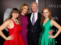 Four adults posing for a formal group photo at a red carpet event on a dark backdrop