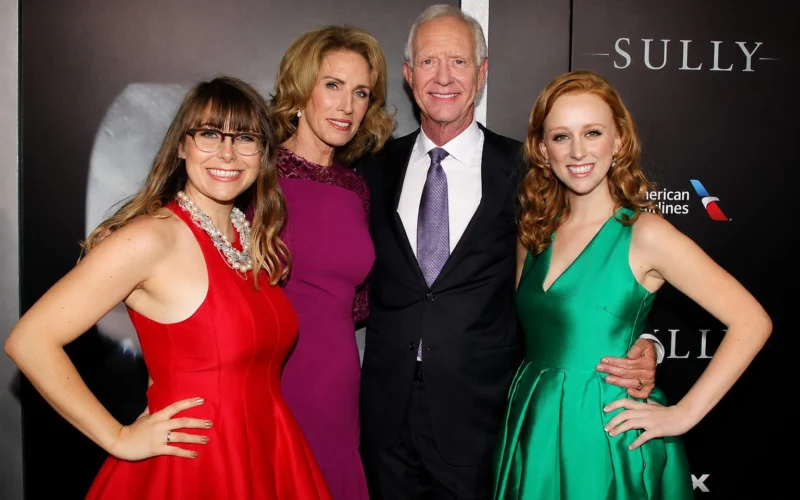 Four adults posing for a formal group photo at a red carpet event on a dark backdrop