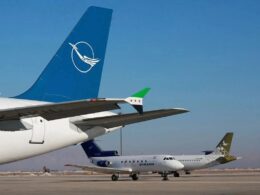 Airplanes parked on a sunny tarmac with a large blue tail fin in the foreground and a Syrian Airlines jet in the midground behind it