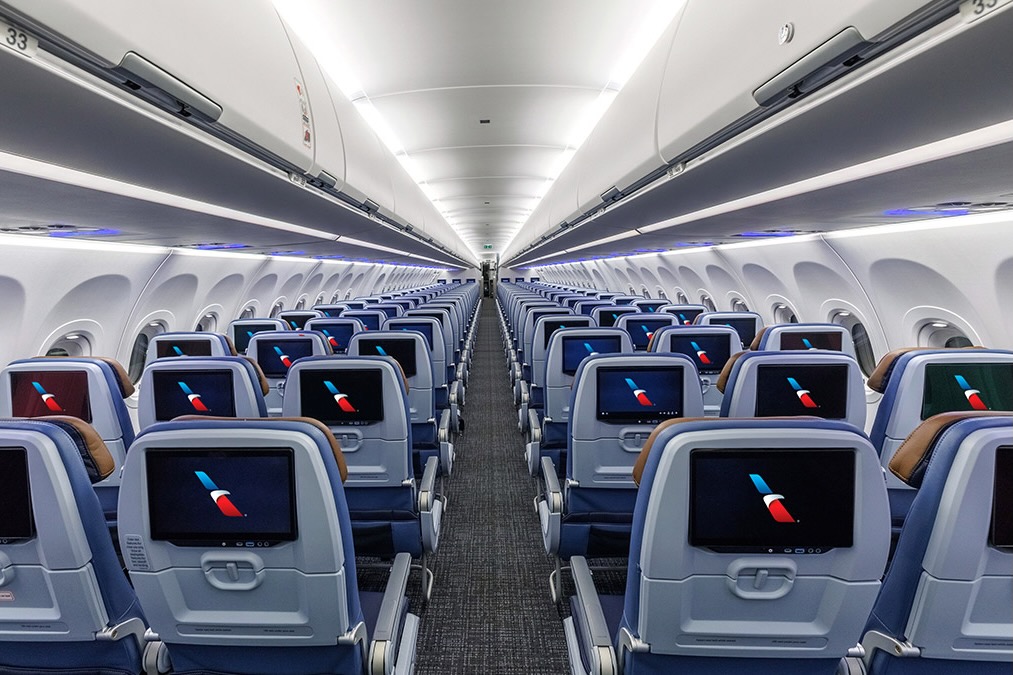 081826 Premium Seatback IFE thumb 1 Interior of a modern passenger jet cabin with rows of blue seats and individual in flight entertainment screens along the backs of the seats viewed down the aisle from the rear