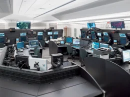 Control room filled with workstations and multiple screens displaying maps and data on their monitors