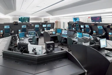 Control room filled with workstations and multiple screens displaying maps and data on their monitors