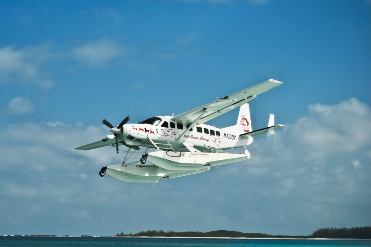 3130DSC 3382 Edit scaled e1733338789143 White twin engine seaplane with outboard floats taking off over blue ocean small island visible in the distance Atlantic Ocean Airways lettering on fuselage