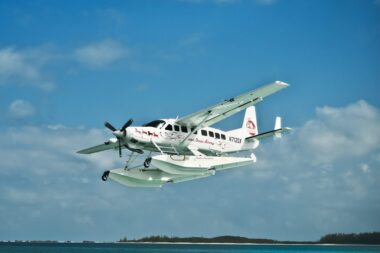 3130DSC 3382 Edit scaled e1733338789143 White twin engine seaplane with outboard floats taking off over blue ocean small island visible in the distance Atlantic Ocean Airways lettering on fuselage