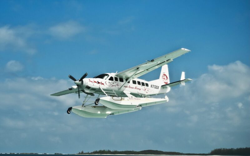 3130DSC 3382 Edit scaled e1733338789143 White twin engine seaplane with outboard floats taking off over blue ocean small island visible in the distance Atlantic Ocean Airways lettering on fuselage