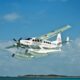 White twin engine seaplane with outboard floats taking off over blue ocean small island visible in the distance Atlantic Ocean Airways lettering on fuselage