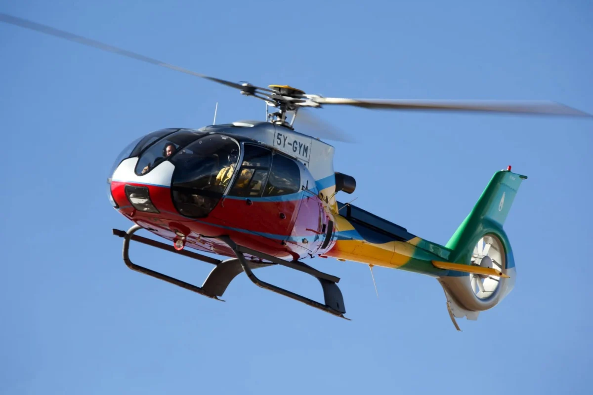 Colorful helicopter in flight with two pilots visible in the cockpit against a clear blue sky