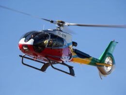 Colorful helicopter in flight with two pilots visible in the cockpit against a clear blue sky