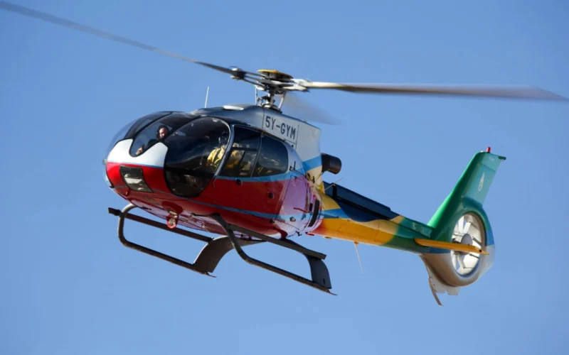 Colorful helicopter in flight with two pilots visible in the cockpit against a clear blue sky