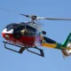 Colorful helicopter in flight with two pilots visible in the cockpit against a clear blue sky