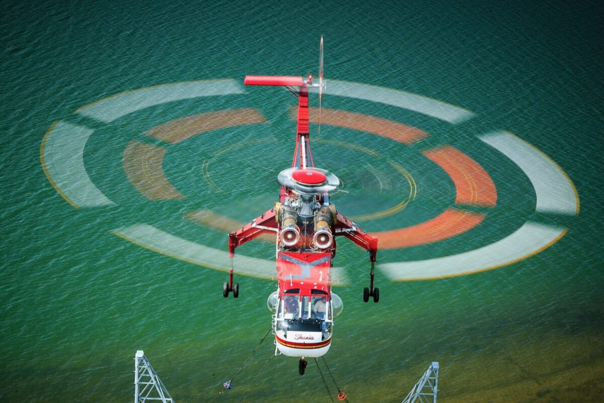 Red rescue helicopter hovering over turquoise water rotor blur forming concentric circles above the sea with a hoist line visible