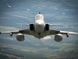 Front view of a fighter jet flying toward the camera over a green valley