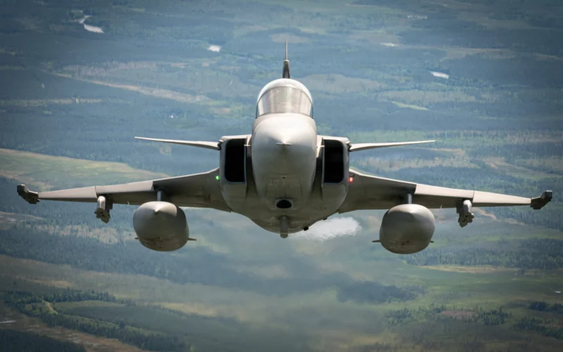 Front view of a fighter jet flying toward the camera over a green valley